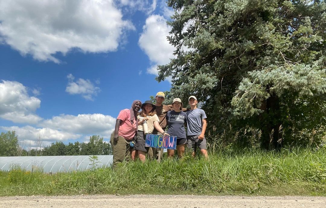 A group of five young men and women stand together in a field. 