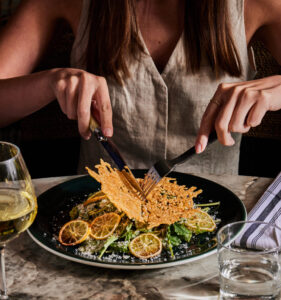 A person with long hair is cutting into salad. 