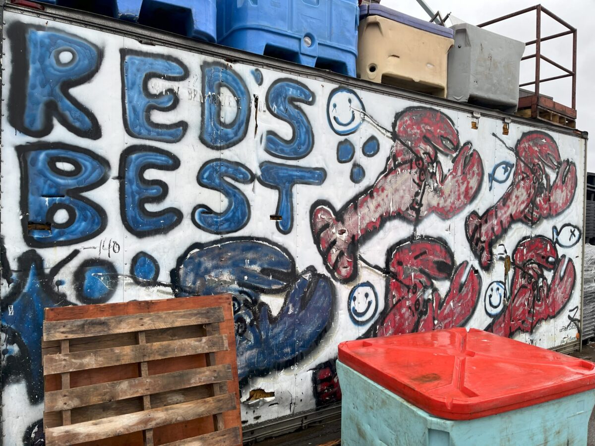 A shipping containre covered in graffiti on a fish pier.